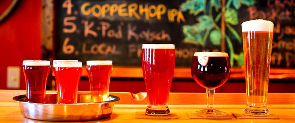 Six glasses of beer sitting on a bar